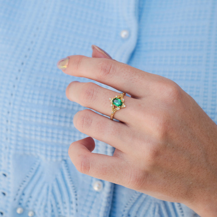 Close-up of hand wearing the Maeve Emerald Couples Ring Set by Aquamarise, featuring a 925-sterling silver ring with 14k yellow gold finish and a radiant emerald gemstone.