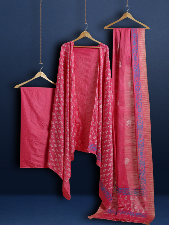 Magenta katan silk unstitched suit set with small white floral hand block print, a solid magenta piece, and a dupatta with wide blue geometric border and metallic-toned edge.