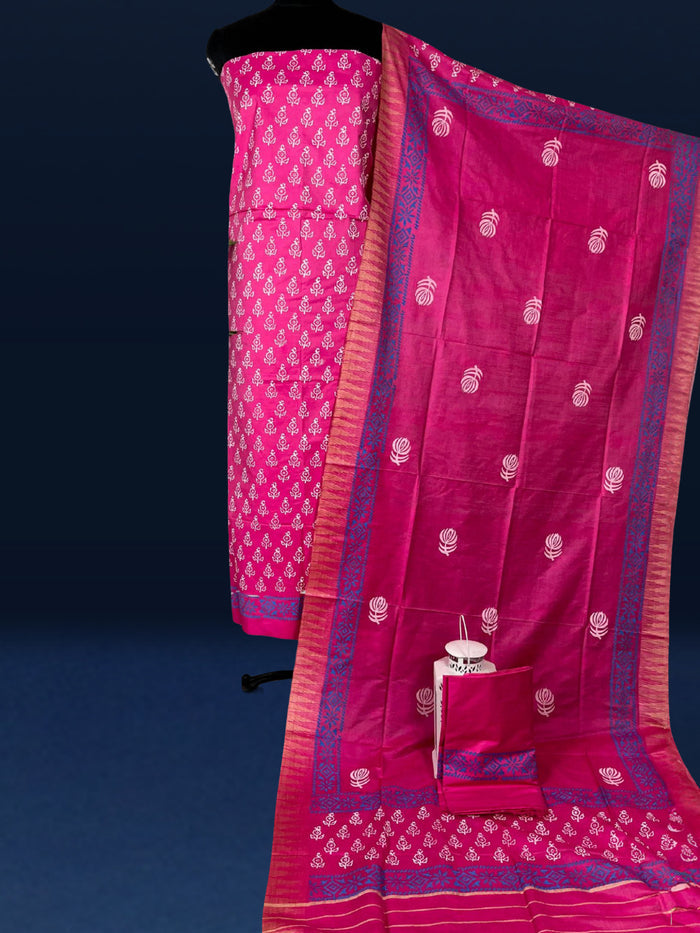 Magenta katan silk unstitched suit set with small white floral hand block print, a solid magenta piece, and a dupatta with wide blue geometric border and metallic-toned edge.