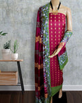 Magenta katan silk unstitched suit set with green block-printed borders of geometric diamonds and abstract botanical shapes, with gold and mustard accents.