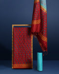 Maroon katan silk unstitched suit set hand block printed with small turquoise botanical motifs and angular geometric key-pattern bands at the ends.