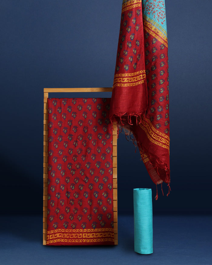 Maroon katan silk unstitched suit set hand block printed with small turquoise botanical motifs and angular geometric key-pattern bands at the ends.
