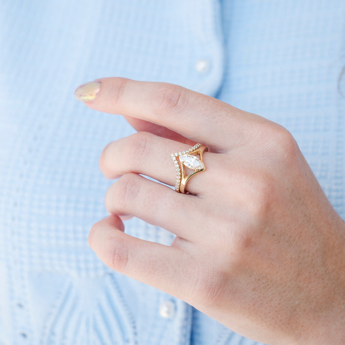 Marquise Cut Lab-Grown Diamond Engagement Ring Set in 14K Solid Yellow Gold (IGI Certified) by Aquamarise Gold, featuring a chevron diamond band paired with a marquise-cut center diamond, showcased on a hand against a light blue textured fabric background.