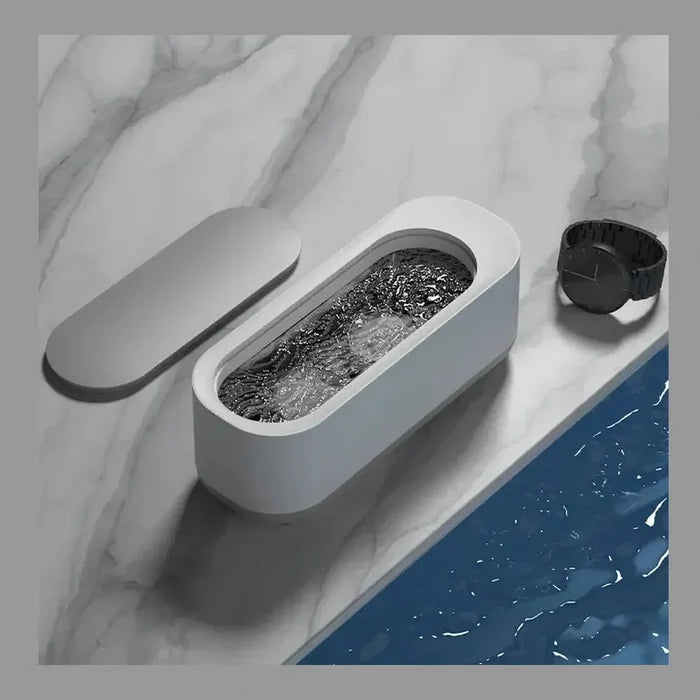Mini Ultrasonic Jewelry Cleaner sitting on a marble surface next to a watch