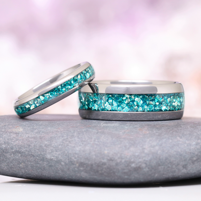 Minimalist Crushed Aquamarine Couples Ring Set by Aquamarise featuring shimmering crushed aquamarine inlays on polished silver bands, captured on a smooth stone surface with a soft pink background.