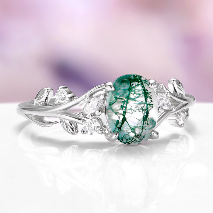 Moss agate engagement ring with leaf design and diamond accent stones over light purple background