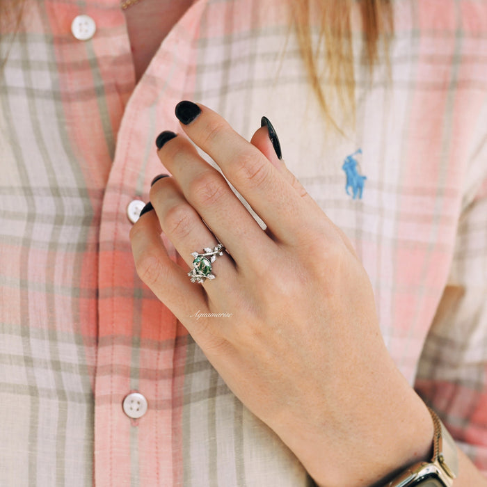 Moss Agate Leaf Couples Ring Set by Aquamarise featuring sterling silver bands with green moss agate stones and leaf details, worn on a hand against a plaid shirt background.
