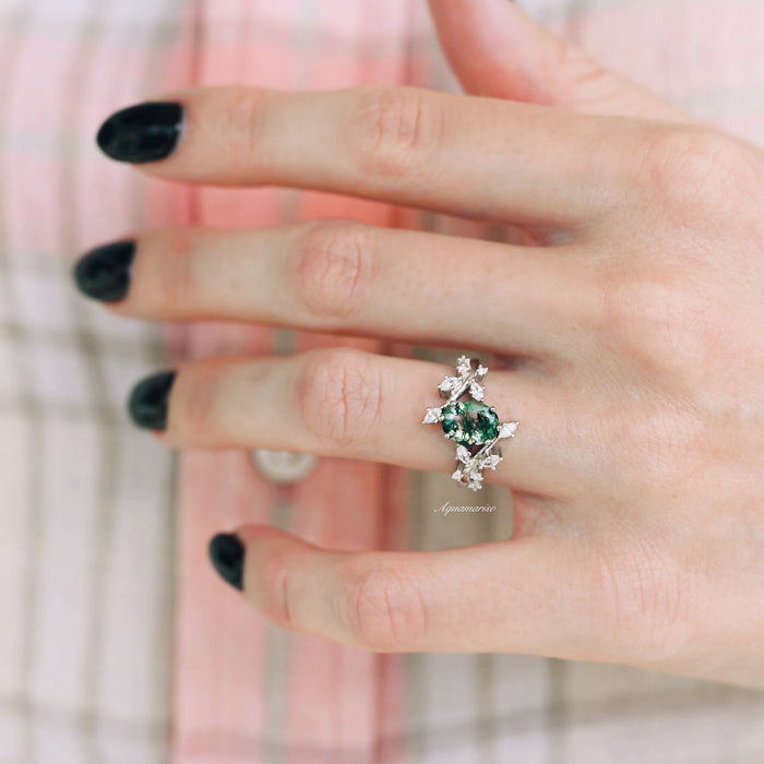Moss Agate Leaf Couples Ring Set by Aquamarise featuring a green moss agate stone surrounded by delicate silver leaf accents, worn on a hand with black nail polish and plaid background.