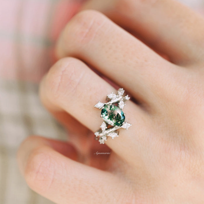 Moss Agate Leaf Couples Ring Set by Aquamarise featuring a sterling silver band with an oval green moss agate stone encircled by delicate leaf-shaped accents, worn on a hand.