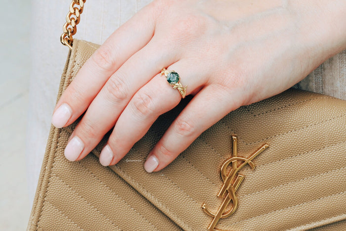 Moss Agate Leaf Ring in 14K Yellow Gold Vermeil by Aquamarise, featuring a round green moss agate stone with intricate leaf details, styled on a hand holding a tan textured purse.