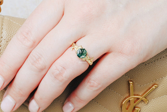 Moss Agate Leaf Ring in 14K Yellow Gold Vermeil by Aquamarise, featuring a deep green moss agate set in a detailed leaf-designed band on a hand holding a tan textured purse.