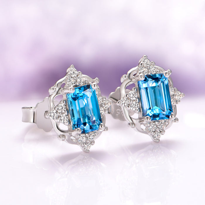 Natural London Blue Topaz Earrings in Sterling Silver featuring emerald-cut blue topaz stones framed by intricate sterling silver and diamond accents by Aquamarise.