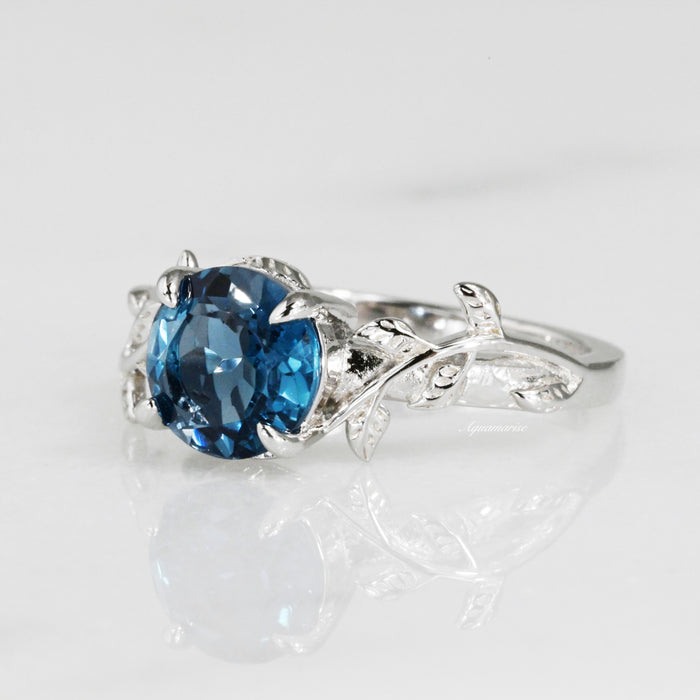 London Blue Topaz Leaf Ring- 14K White Gold by Aquamarise Gold featuring a natural deep blue topaz set in a delicately crafted white gold band with nature-inspired leaf and vine accents.