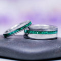 Two silver rings with green gemstone inlays on a gray surface with a purple gradient background.