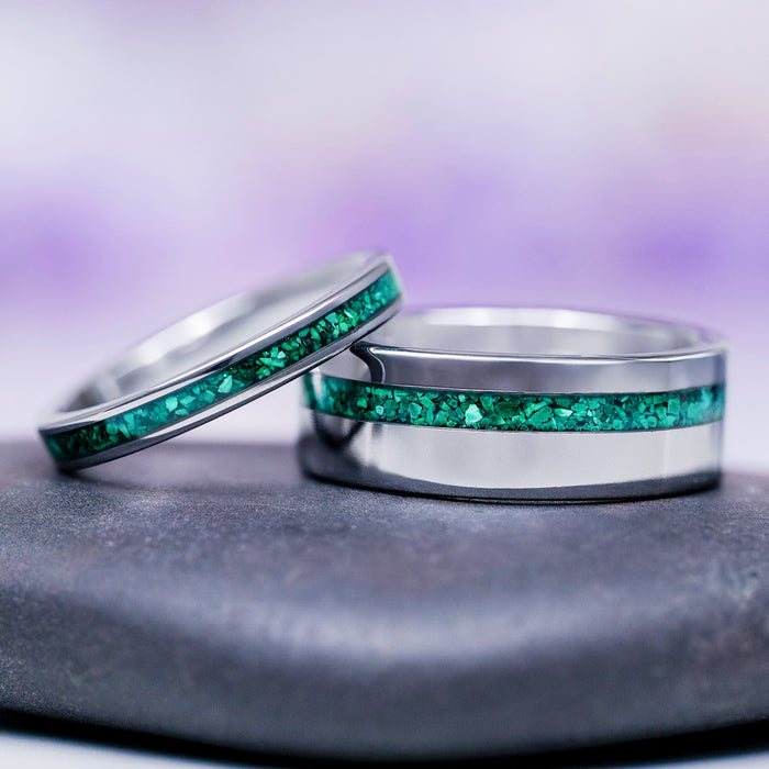 Two silver rings with green gemstone inlays on a gray surface with a purple gradient background.