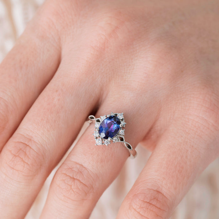 Silver ring with a blue gemstone on a person's finger against a neutral background