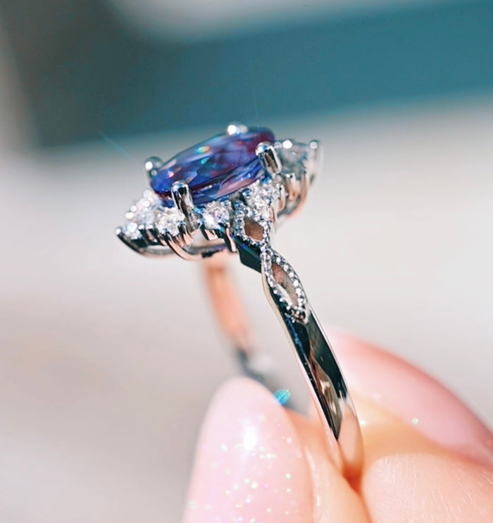 Close-up of a silver ring with a blue gemstone held by a hand.