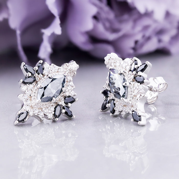 Nightbriar gray moissanite and black onyx stud earrings on a mirror, marquise centers with black onyx rays and cubic zirconia halos