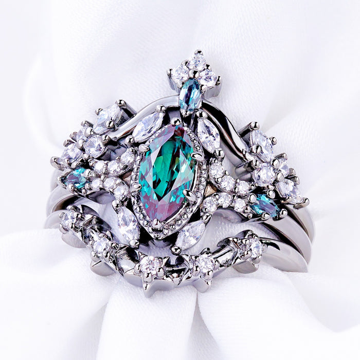 Nightbriar alexandrite bridal ring set in black ruthenium stacked on white satin, marquise center with starburst halo and two contour bands