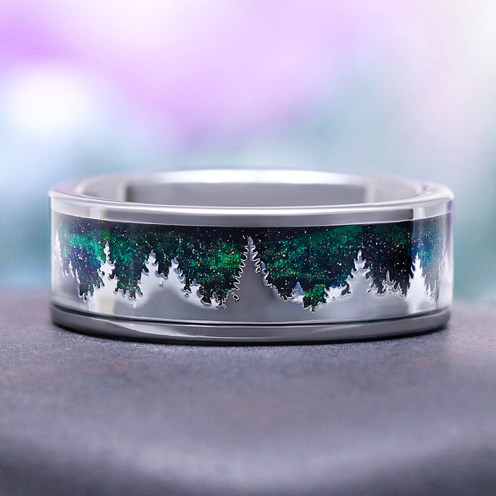 Northern Lights Pines men's 8mm tungsten wedding band with green goldstone and blue sandstone inlay beneath a polished pine forest silhouette by Aquamarise