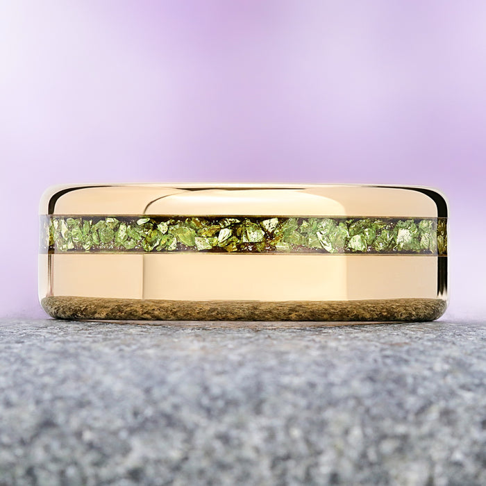 Crushed peridot gold tungsten wedding band on granite, showing the olive-green flakes against the mirror-polished gold