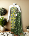 Olive green Katan silk unstitched suit set printed with a white vine and paisley pattern, yellow and terracotta accents and a chevron band at the hem