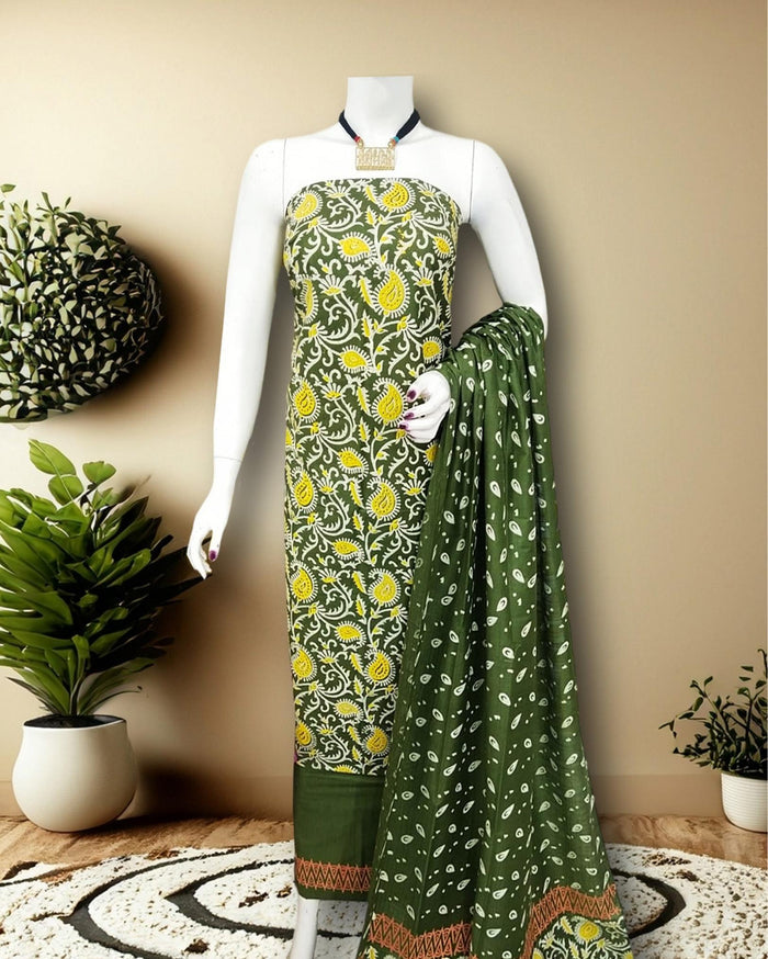 Olive green Katan silk unstitched suit set printed with a white vine and paisley pattern, yellow and terracotta accents and a chevron band at the hem