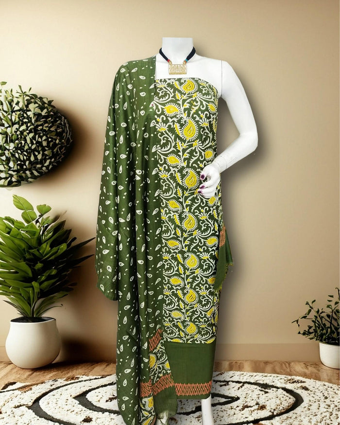 Olive green Katan silk unstitched suit set printed with a white vine and paisley pattern, yellow and terracotta accents and a chevron band at the hem