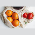 Organic cotton reusable produce bags holding oranges and tomatoes, perfect for eco-friendly shopping.