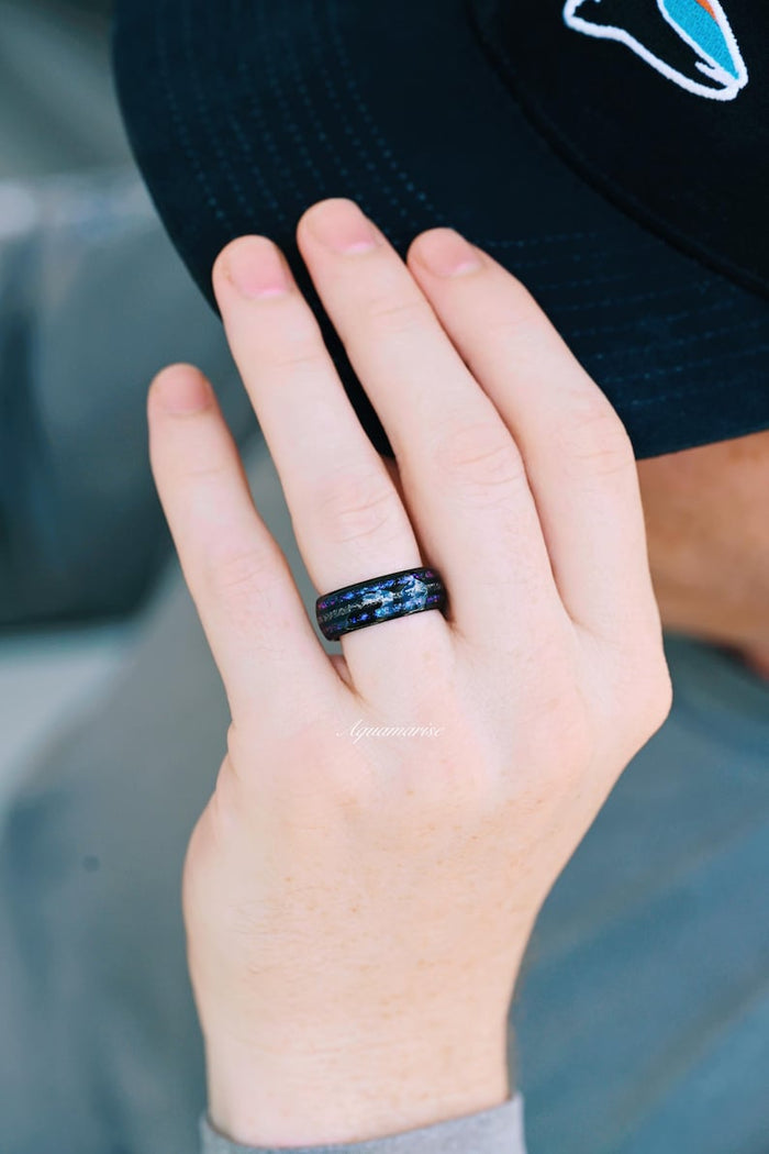 Faye Galaxy Orion Nebula™ & Sapphire Couples Ring Set featuring a black finish band inlaid with shimmering blue sapphire flakes, styled on a hand wearing a casual dark cap, part of Aquamarise’s Matching Couples' Rings and Orion Nebula Rings® collections.