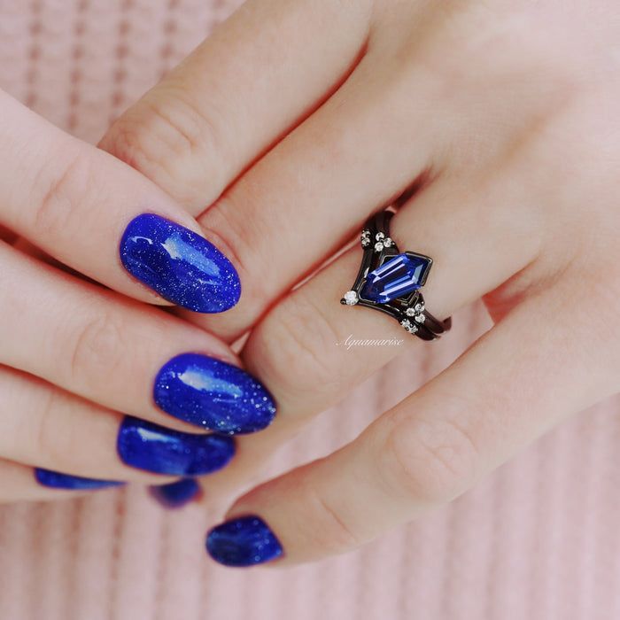 Orion Nebula™ & Tanzanite Couples Ring Set by Aquamarise featuring a faceted blue tanzanite gemstone and black band with diamond accents on a hand with sparkling blue nails.