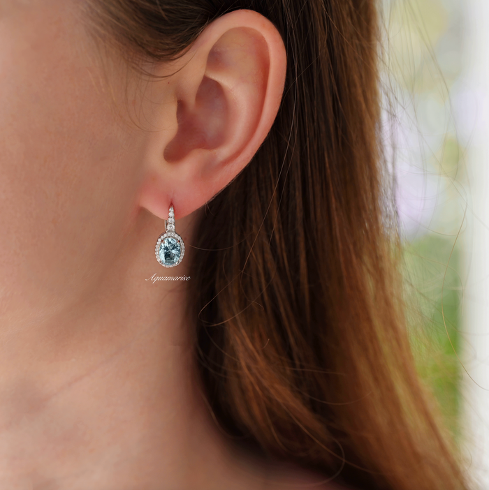 Oval Aquamarine Drop Earrings in Sterling Silver worn on a woman's ear, featuring aquamarine stones surrounded by sparkling simulated diamonds by Aquamarise.