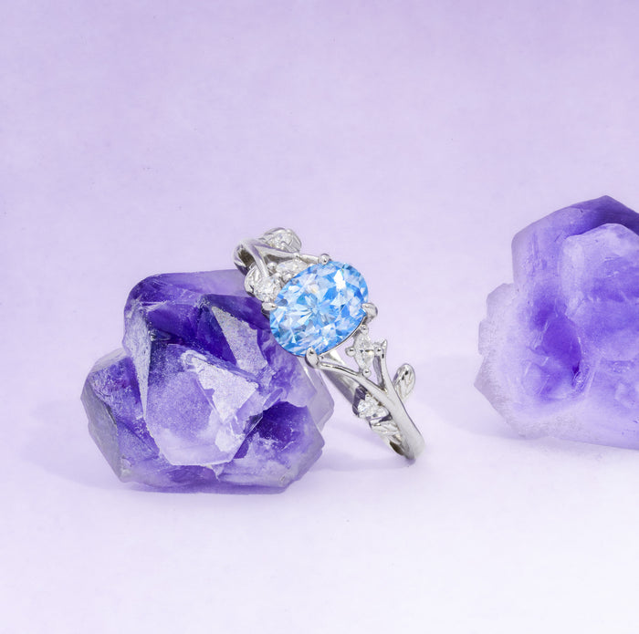 Silver ring with a blue gemstone and purple crystal on a light purple background