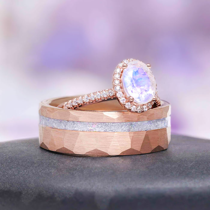 Oval Rainbow Moonstone Couples Ring Set by Aquamarise featuring a faceted rose gold band with silver inlay and a halo ring with an iridescent moonstone surrounded by small diamonds.