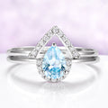 Silver ring with a blue teardrop gemstone on a light purple background