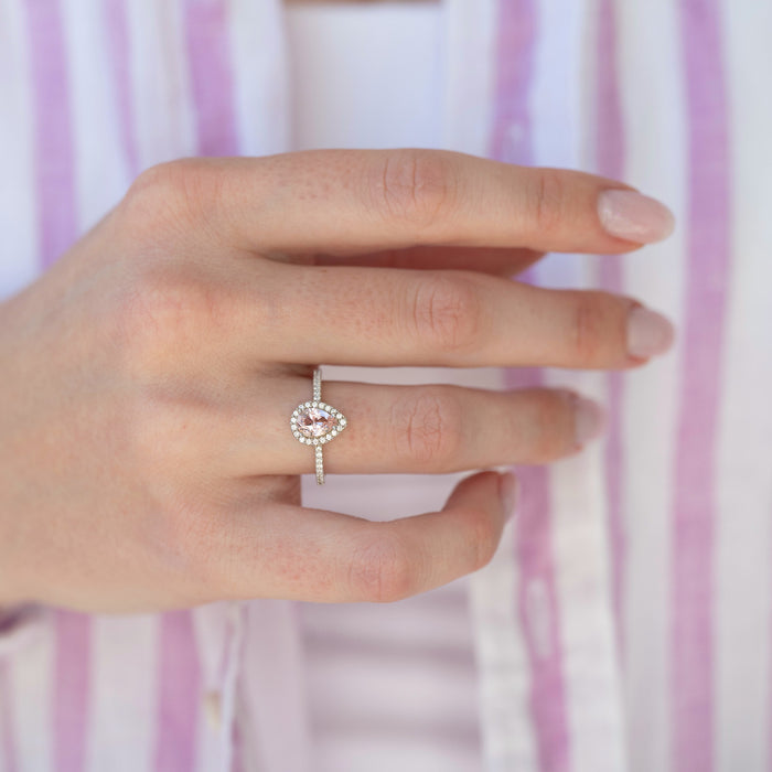 Hand wearing a silver ring with a pink gemstone against a striped background