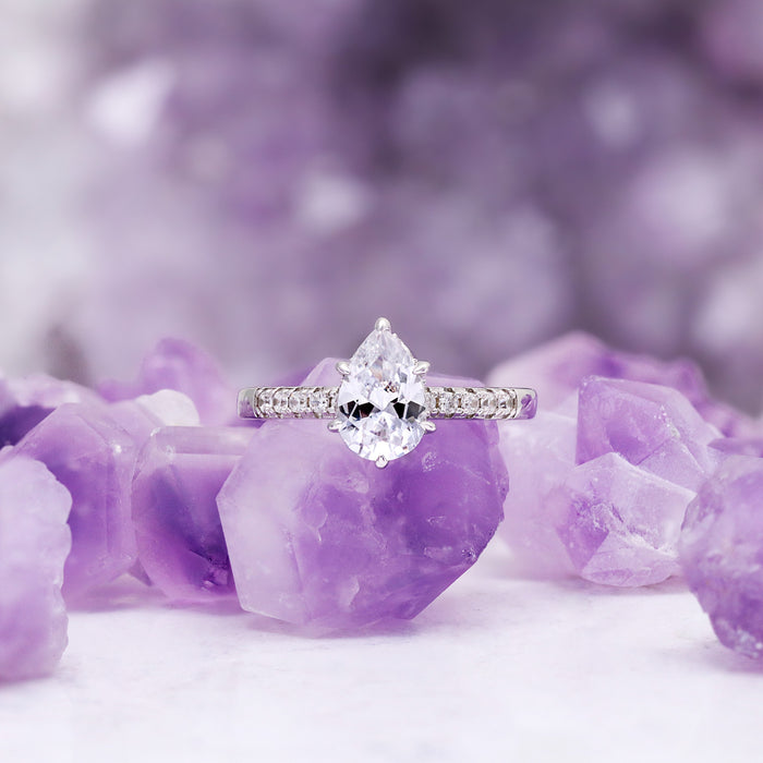 Pear White Sapphire Art Deco Bridal Ring Set in Sterling Silver displayed on purple crystal stones, showcasing sparkling pear-shaped white sapphire with delicate sterling silver band by Aquamarise.