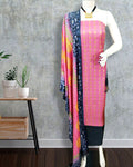 Unstitched pink Katan silk suit set with vertical rows of small geometric block print on the top and a dupatta of large black floral and geometric panels edged with decorative geometric bands.