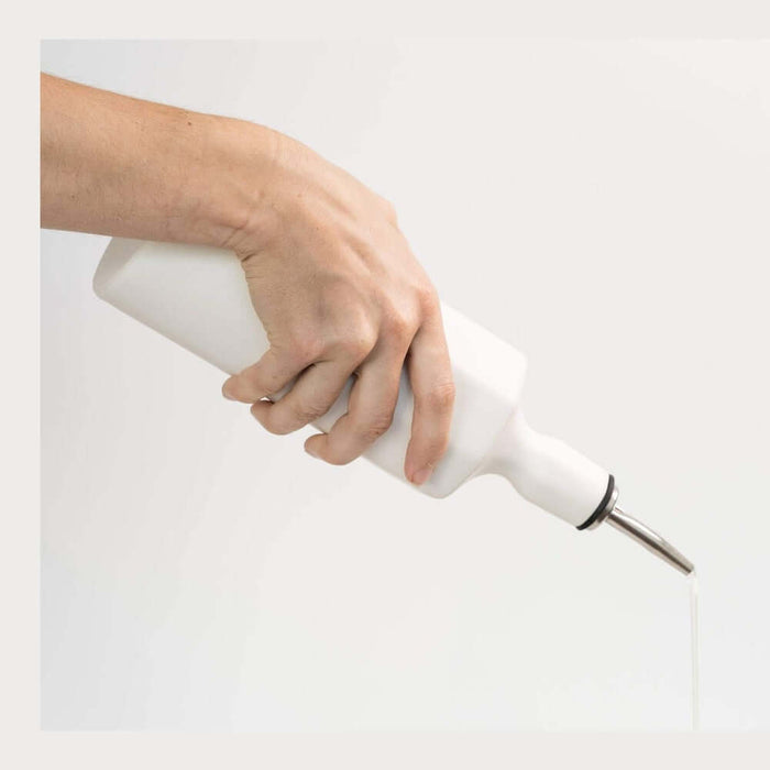 Hand pouring from a handcrafted porcelain olive oil dispenser with a sleek spout.