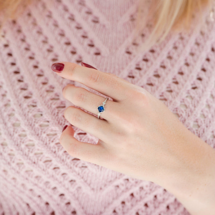 Hand wearing a ring with a blue gemstone on a pink textured fabric background