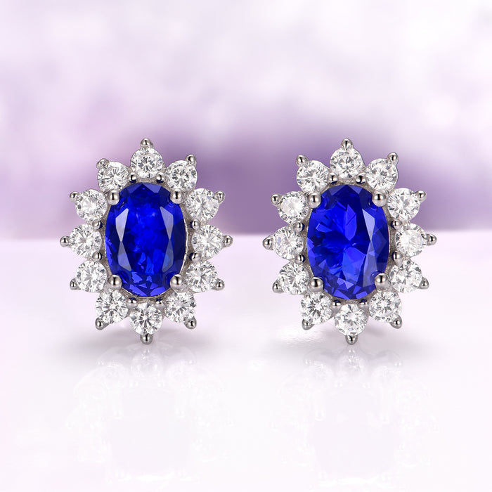 Princess Diana Blue Sapphire Stud Earrings in Sterling Silver by Aquamarise, featuring deep blue oval sapphires surrounded by sparkling simulated diamonds on polished silver settings.
