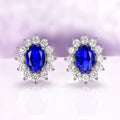 Princess Diana Blue Sapphire Stud Earrings in Sterling Silver by Aquamarise, featuring deep blue oval sapphires surrounded by sparkling simulated diamonds on polished silver settings.