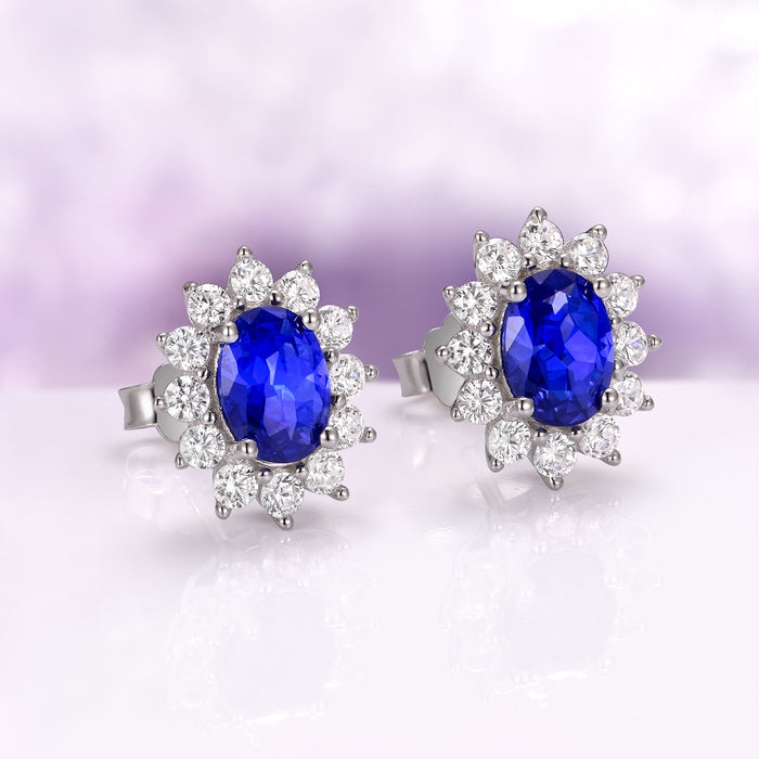 Princess Diana Blue Sapphire Stud Earrings in Sterling Silver by Aquamarise, showcasing deep blue oval sapphires framed by sparkling simulated diamonds on polished sterling silver settings.