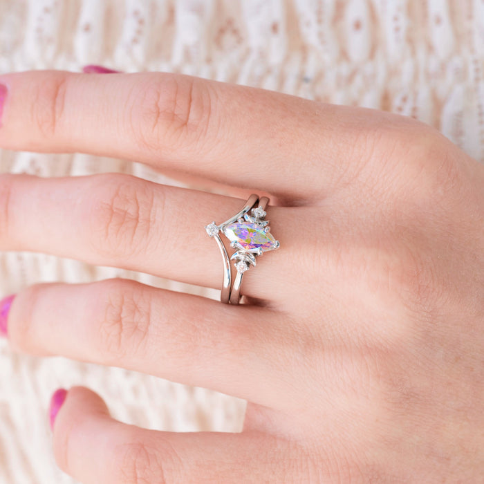 Silver engagement ring set with marquise cut rainbow moissanite center stone and diamond accents on hand over a light background