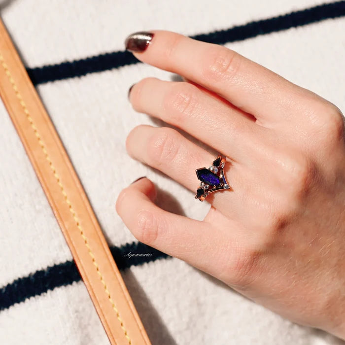 Galaxy Sandstone Starry Night Couples Ring Set by Aquamarise featuring a unique deep blue sandstone gemstone in a rose gold band, styled on a hand with natural light and striped fabric background.