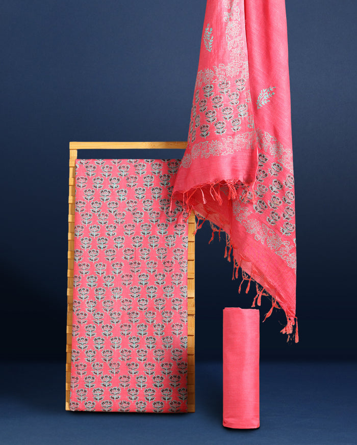 Vibrant pink katan silk unstitched suit set hand block printed with grey and white floral motifs, shown with a fringed dupatta carrying a decorative band.
