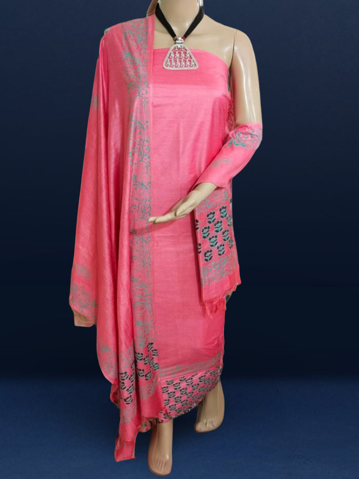 Vibrant pink katan silk unstitched suit set hand block printed with grey and white floral motifs, shown with a fringed dupatta carrying a decorative band.