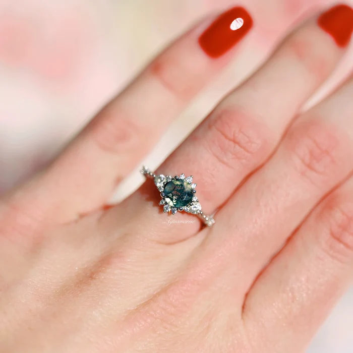 Round Green Moss Agate Ring in Sterling Silver by Aquamarise featuring a round green moss agate stone with vintage-inspired diamond accents on a polished silver band worn on a hand with red nails.
