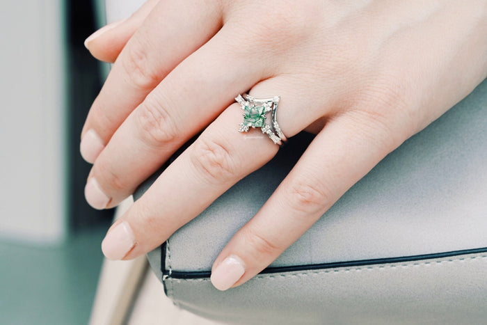 Princess Cut Moss Agate Engagement Ring Set in 14K White Gold by Aquamarise Gold, featuring a unique green moss agate center with diamond accents on a hand resting on a light gray purse.