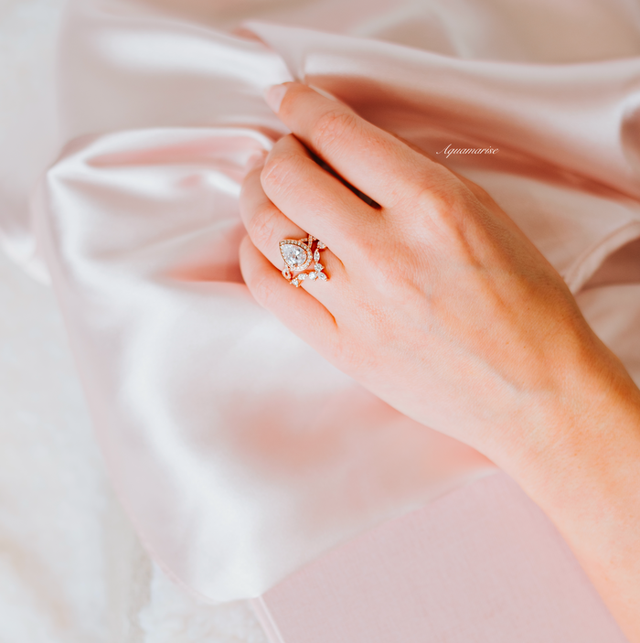 Woman's hand resting on pink satin fabric showcasing the Nouveau Diamond (cz) Engagement Ring Set- 14K Rose Gold Vermeil by Aquamarise, elegant rose gold pavé twisted vine design.